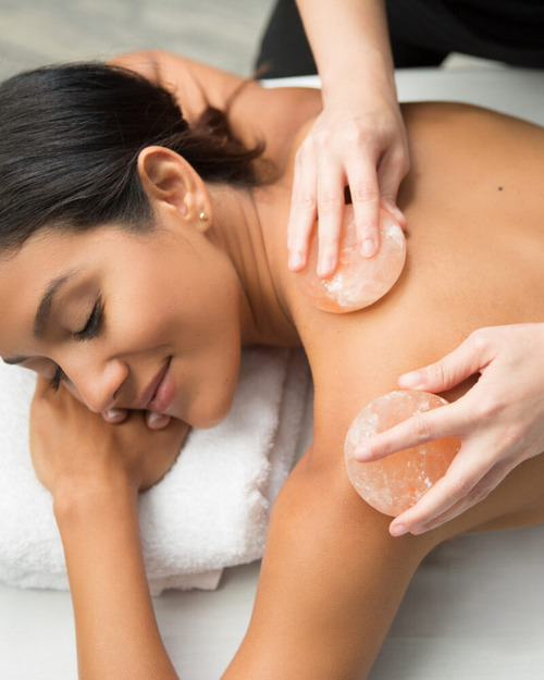 Person lying down with eyes closed, receiving a back massage using smooth stones.